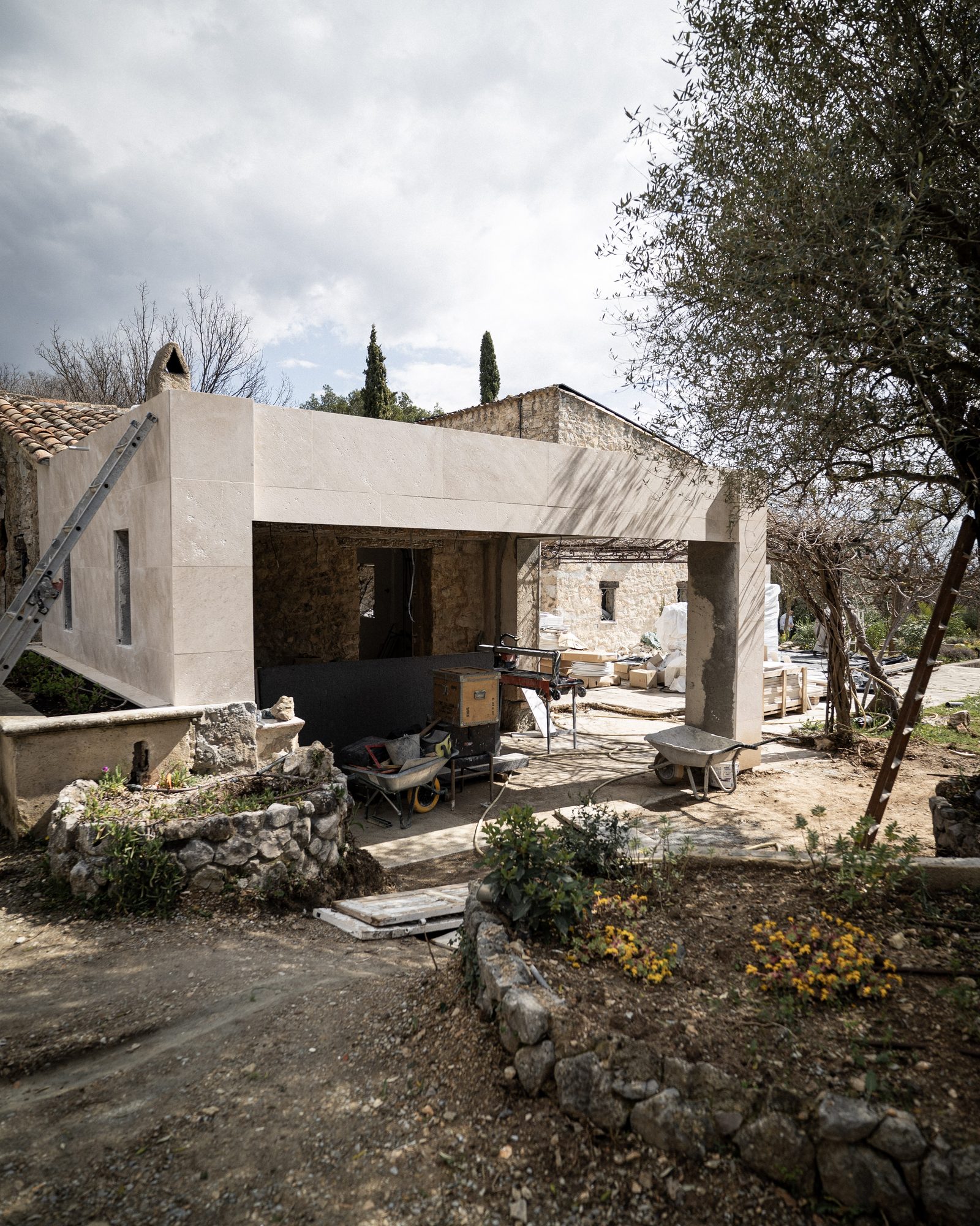 The new stone-clad extension under construction, framed by an ancient olive tree